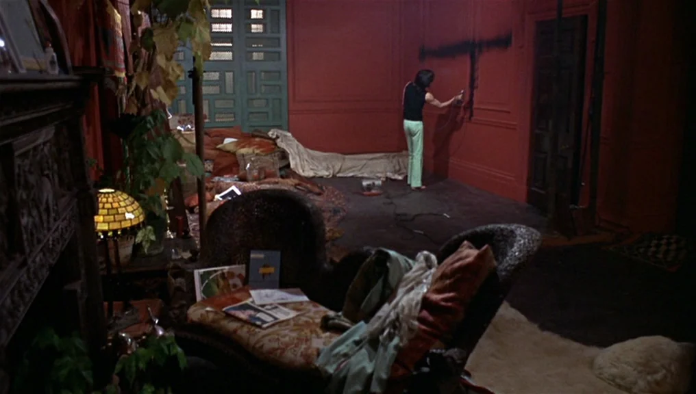 Performance (1970) movie still: wide — An interior space with deep red walls features scattered textiles and a central wooden armchair. A woman…