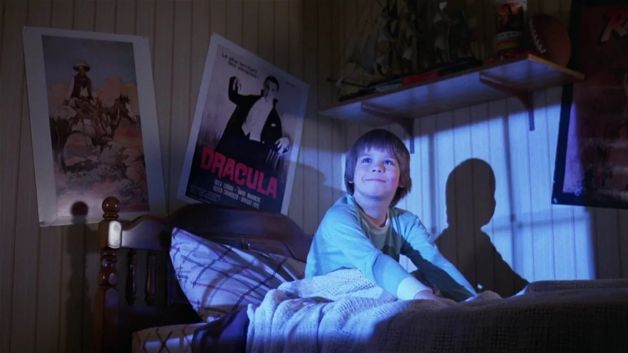 Creepshow (1982) movie still: medium — A dimly lit room features walls decorated with posters of Dracula and a cowboy. A young boy sits upright in a…