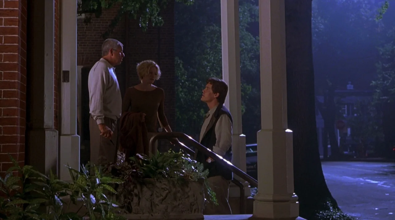 Hollow Man (2000) movie still: fullbody — Three people stand together on the elevated wooden deck of a brick house at night. They are engaged in a…