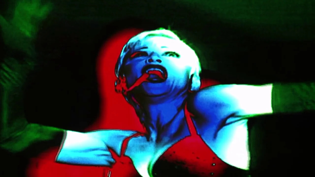 Naqoyquatsi (2002) movie still: closeup — A dark space lit with intense primary-colored lighting effects. A woman with short blonde hair sings with…