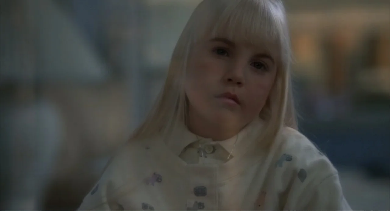 Poltergeist III (1988) movie still: closeup — A child sits in a softly lit interior space with muted colors. The child faces the camera with a…