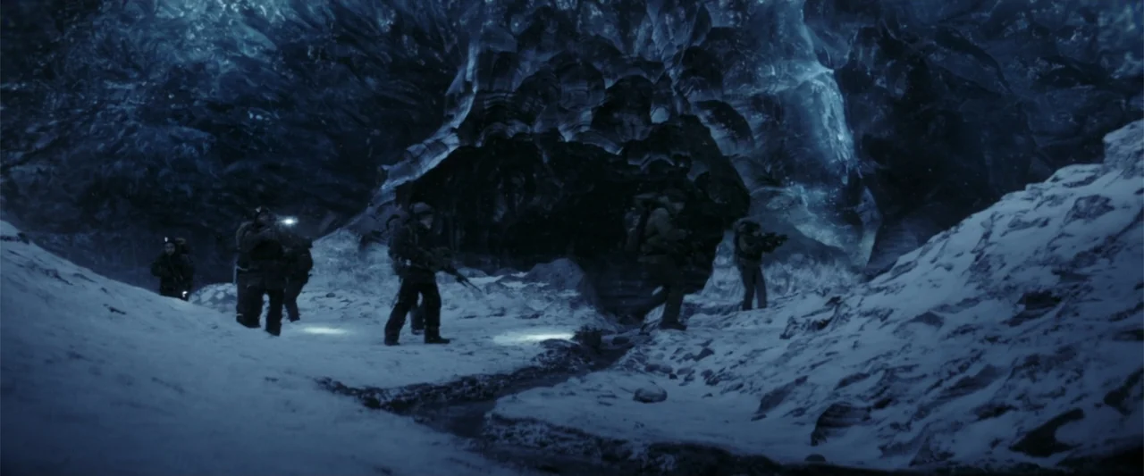 The Tomorrow War (2021) movie still: wide — A group of figures in tactical gear navigate a dark, cavernous ice environment at night. Snow coats the…