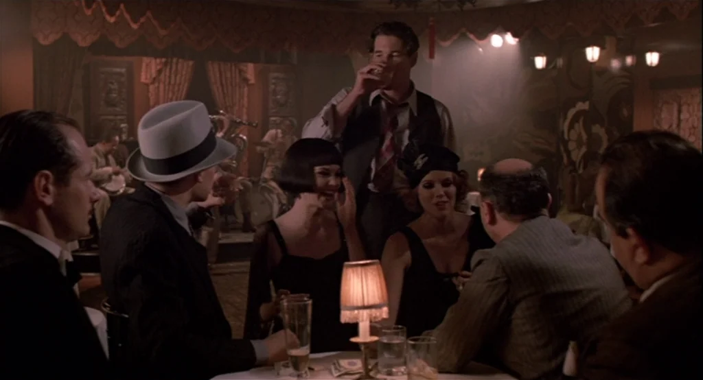 The Cotton Club (1984) movie still: medium — A dimly lit nightclub with vintage decor and warm table lamps on round tables. A small group of people…