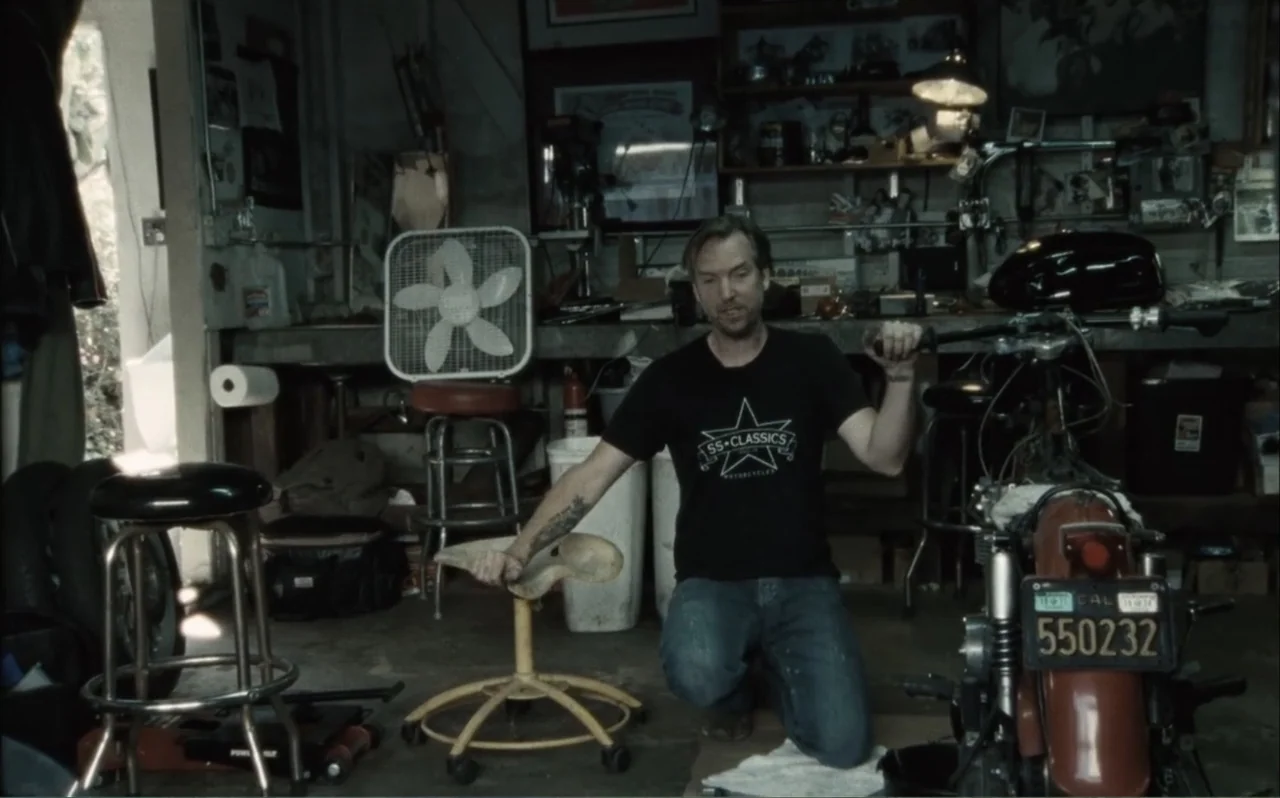The Greasy Hands Preachers (2014) movie still: medium — A cluttered home garage contains various tools, mechanical parts, and a motorcycle being…