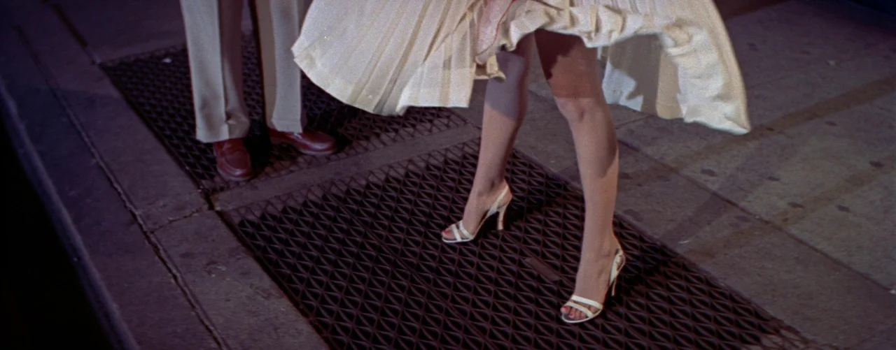 The Seven Year Itch (1955) movie still: closeup — A metal subway grate on a city sidewalk at night with two people standing. A white dress blows…