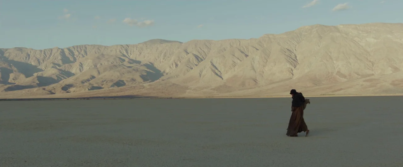 Last Days in the Desert (2015) movie still: wide — A vast, flat, cracked desert landscape stretches out toward a range of barren mountains. A lone…