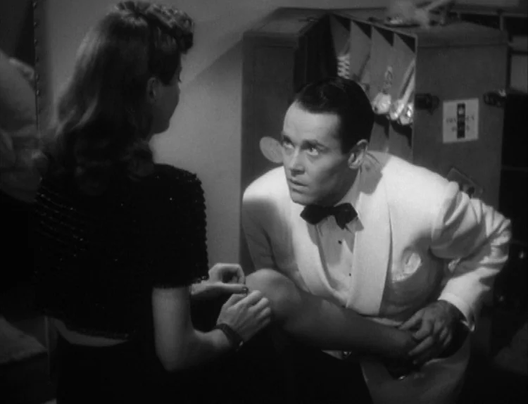 The Lady Eve (1941) movie still: medium — A dimly lit dressing room contains a shoe storage rack in the background. A man kneels before a woman to…