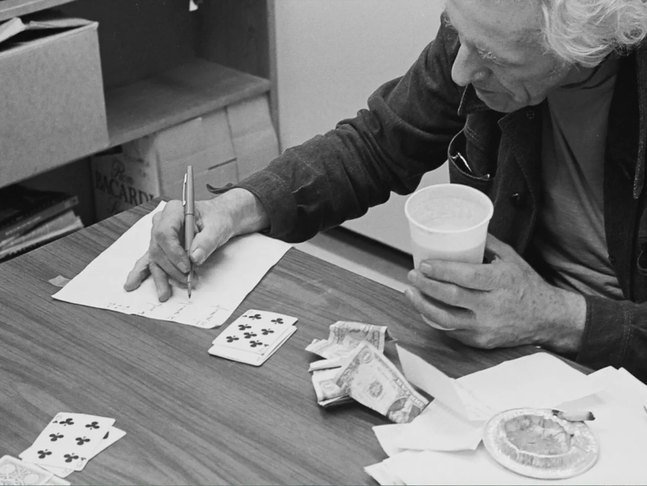 Don't Expect Too Much (2011) movie still: medium — A cluttered wooden desk holds playing cards, loose paper money, and an aluminum ashtray. An…