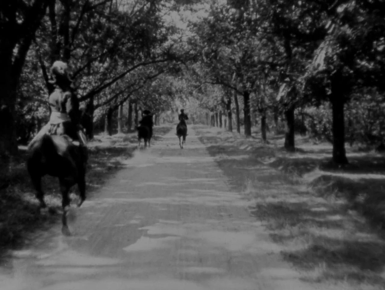 Napoleon (1927) movie still: wide — A dirt road stretches into the distance, framed by rows of dense, leafy trees. Three individuals ride their…