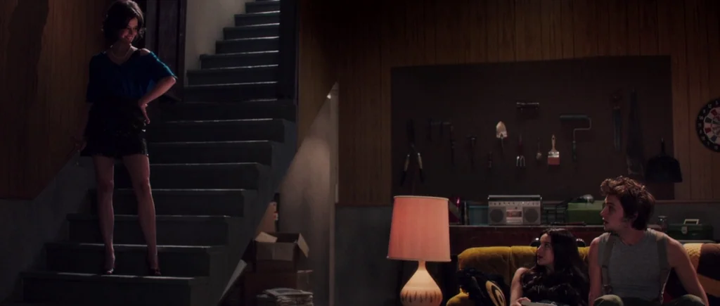 White Bird in a Blizzard (2014) movie still: wide — A basement with wood-paneled walls and a pegboard display of hand tools. A woman stands on…