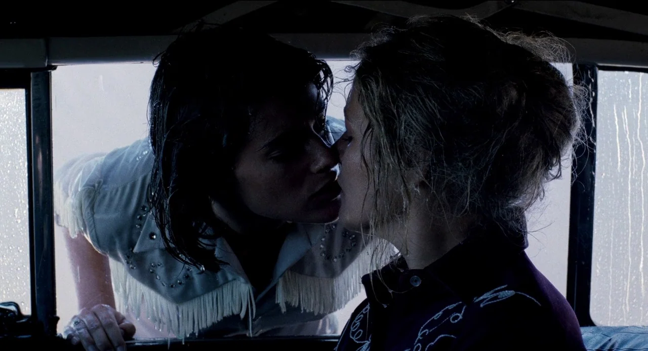Desert Hearts (1985) movie still: medium — A close view through a vehicle window shows two women leaning in to kiss. They are framed against a…