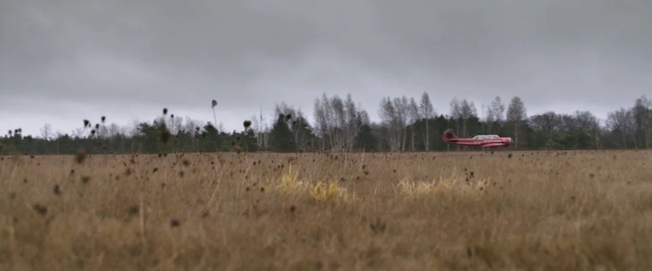 Resident Evil: Afterlife (2010) movie still: wide — A vast, dry grass field extends toward a dense line of distant trees. A small red airplane rests…