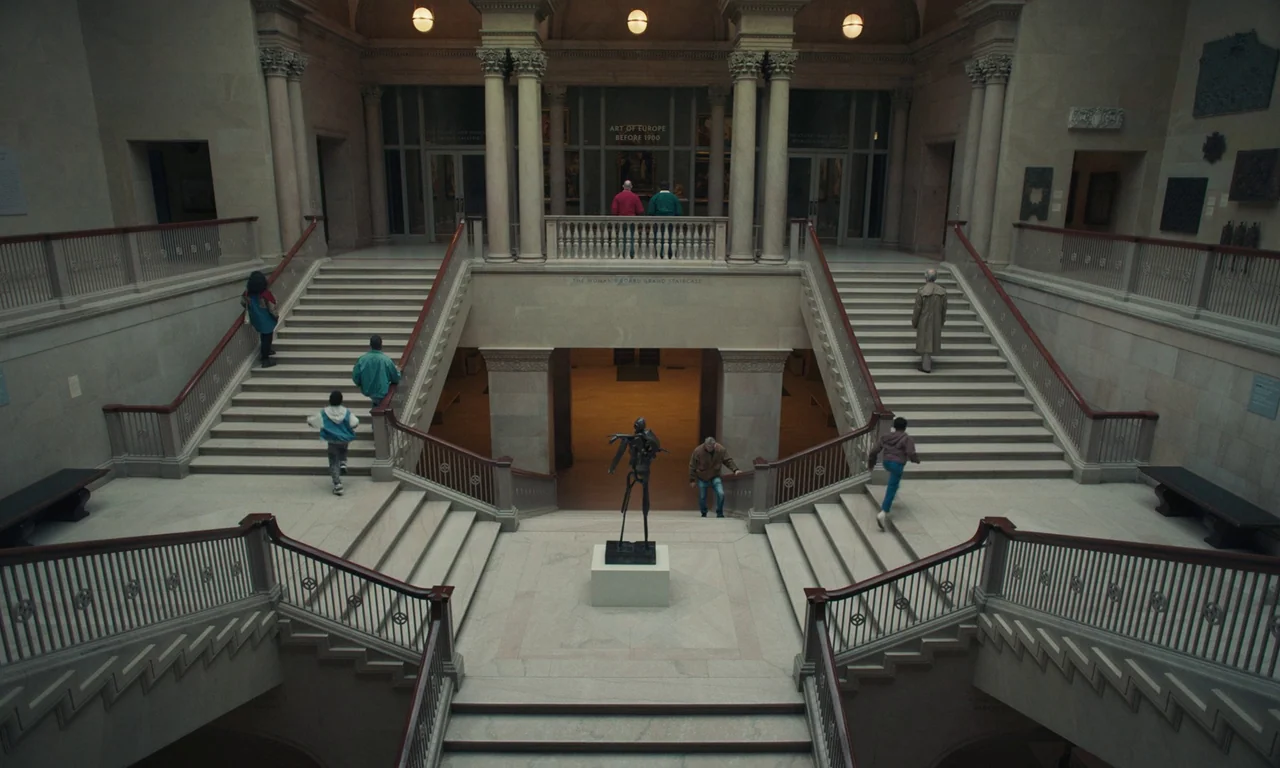 We Grown Now (2023) movie still: establishing — A grand, symmetrical limestone museum staircase with bronze railings features an abstract sculpture…