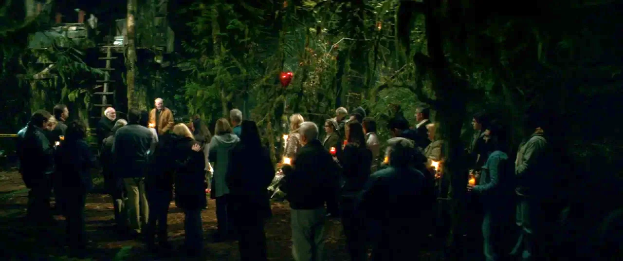 Horns (2013) movie still: wide — A group of people gathers in a dark forest at night among mossy trees. They stand in a circle holding small candles…