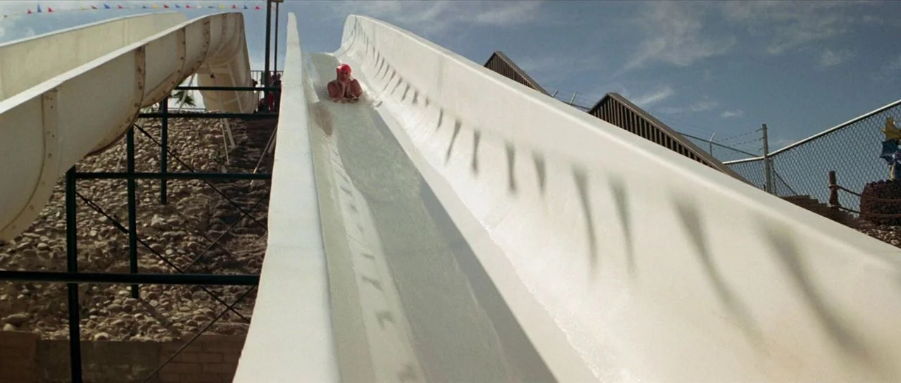 Bill and Ted’s Excellent Adventure (1989) movie still: wide — A white plastic water slide descends from an elevated platform into an outdoor park. A…