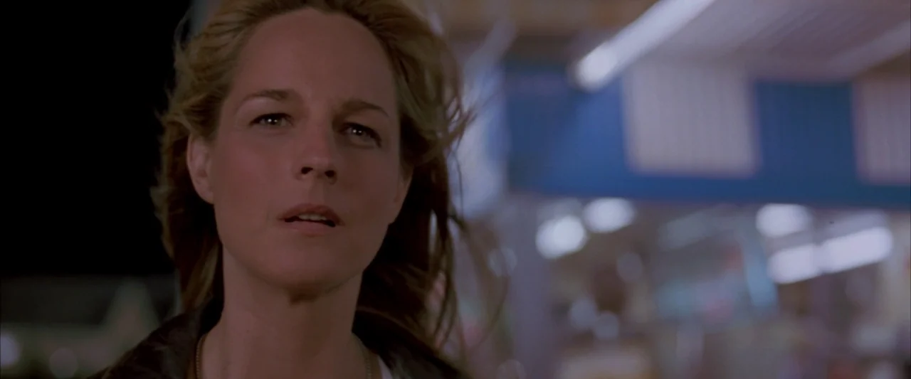 Twister (1996) movie still: closeup — A nighttime scene at a dimly lit outdoor gas station with a blurred canopy overhead. A woman with blonde hair…