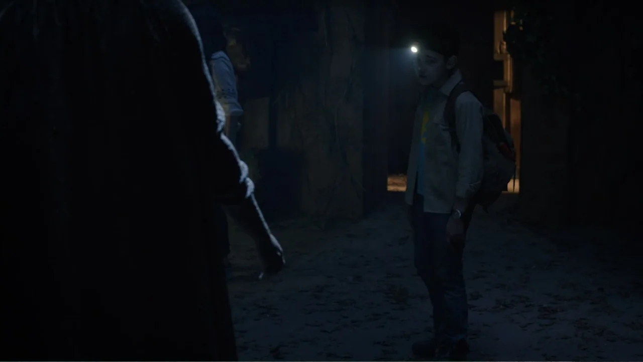Legends of the Hidden Temple (2016) movie still: medium — A dim outdoor space at night with scattered leaves on the ground. A young boy wears a…