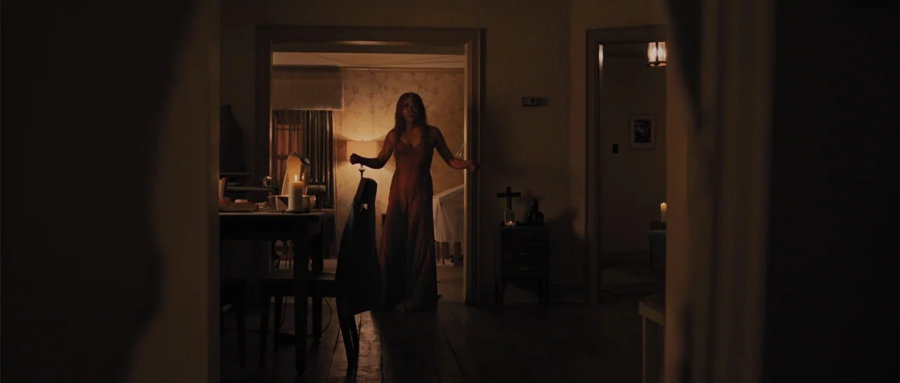 Carrie (2013) movie still: fullbody — The interior shows two connected rooms with floral wallpaper and dim artificial light. A woman in a slip dress…