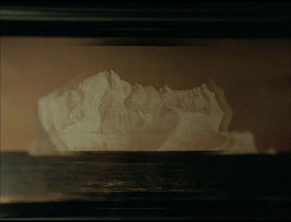 Post Tenebras Lux (2012) movie still: closeup — A dark framed picture showing a textured, pale illustration of a mountain range. The painting is set…