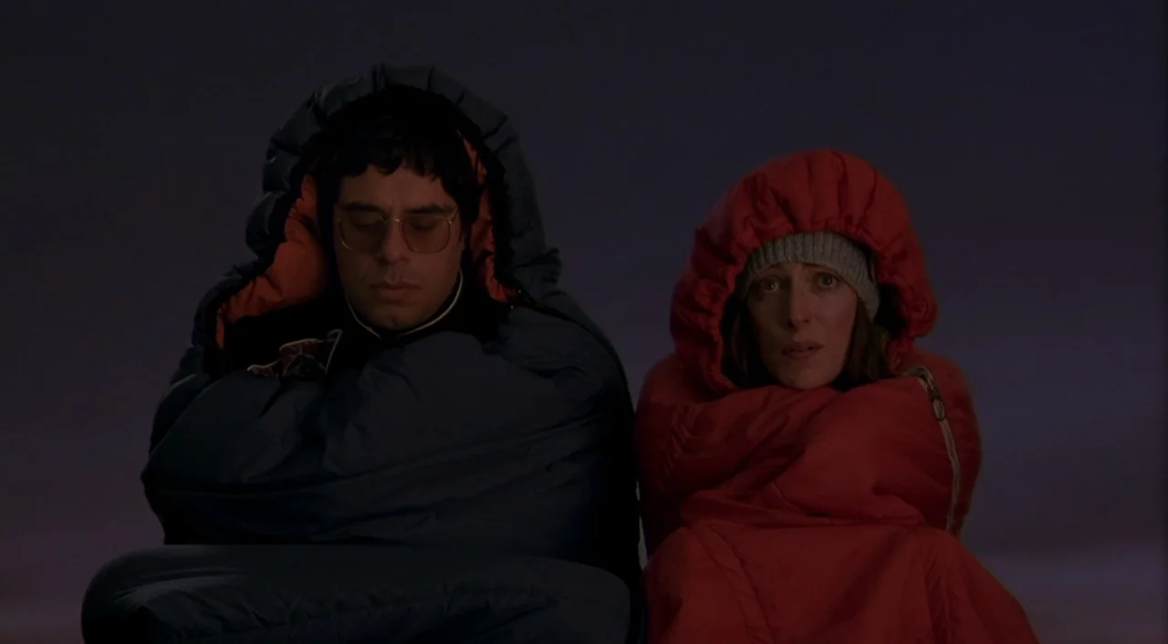 Eagle Vs. Shark movie still: medium — Two individuals sit in a pitch-black outdoor space wrapped in thick sleeping bags. They remain stationary…