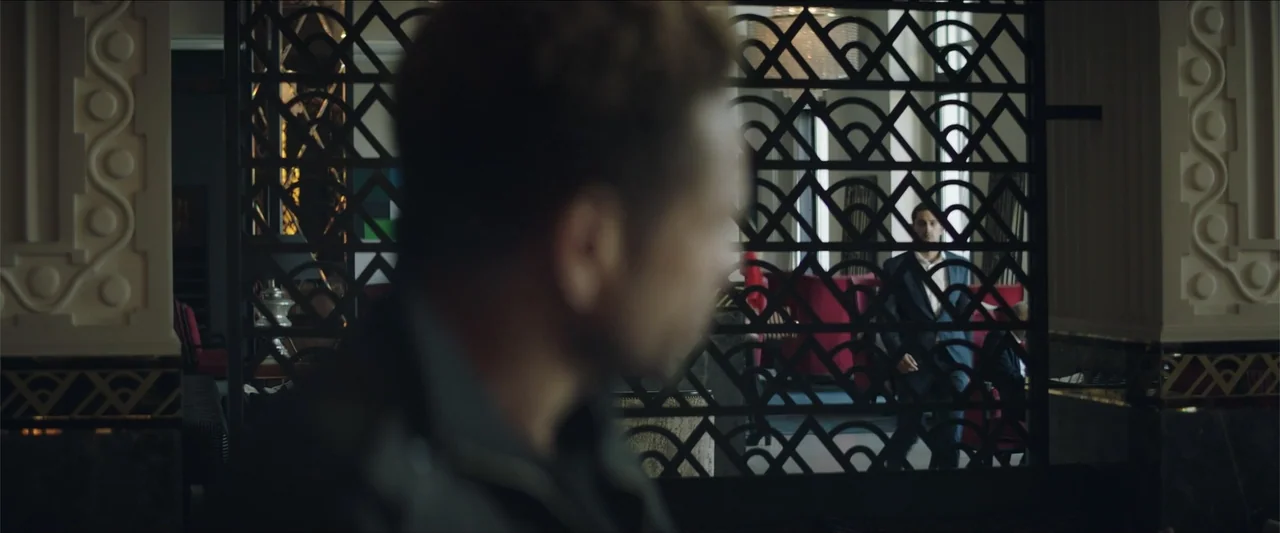 Redemption Day (2021) movie still: medium — An upscale hotel lobby features a large, dark, ornate geometric metal room divider. A man in a suit…