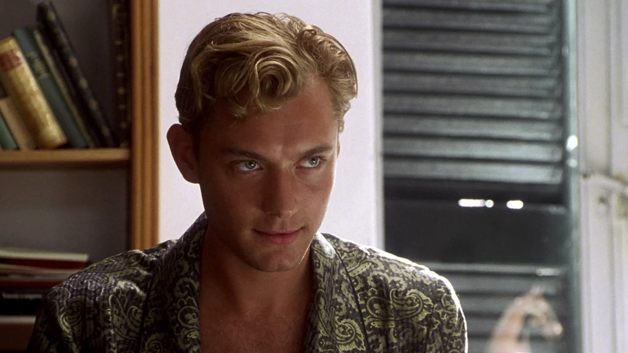 The Talented Mr. Ripley (1999) movie still: closeup — A man sits in a study with a bookshelf visible on the left side. He wears a paisley-patterned…