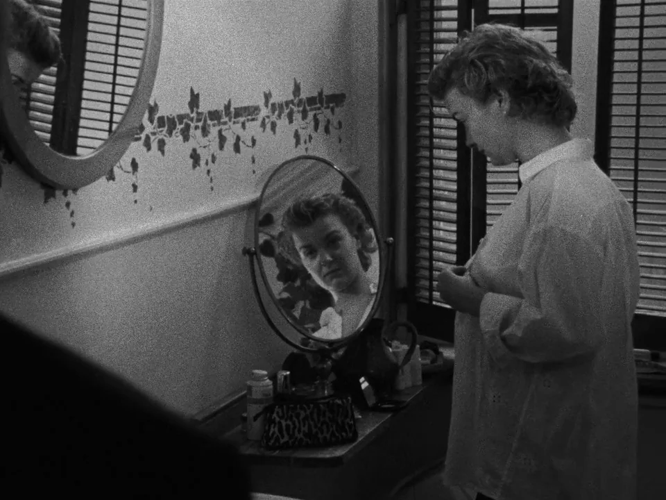 Following (1998) movie still: medium — A vintage bathroom features walls decorated with vine stencils and circular vanity mirrors. A young woman in…
