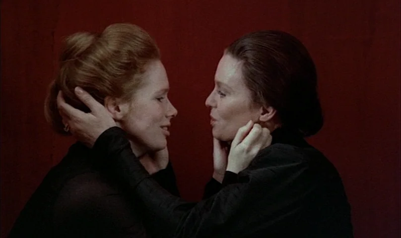 Cries and Whispers (1972) movie still: medium — Two women stand against a solid, dark red wall in an interior space. They face each other with their…