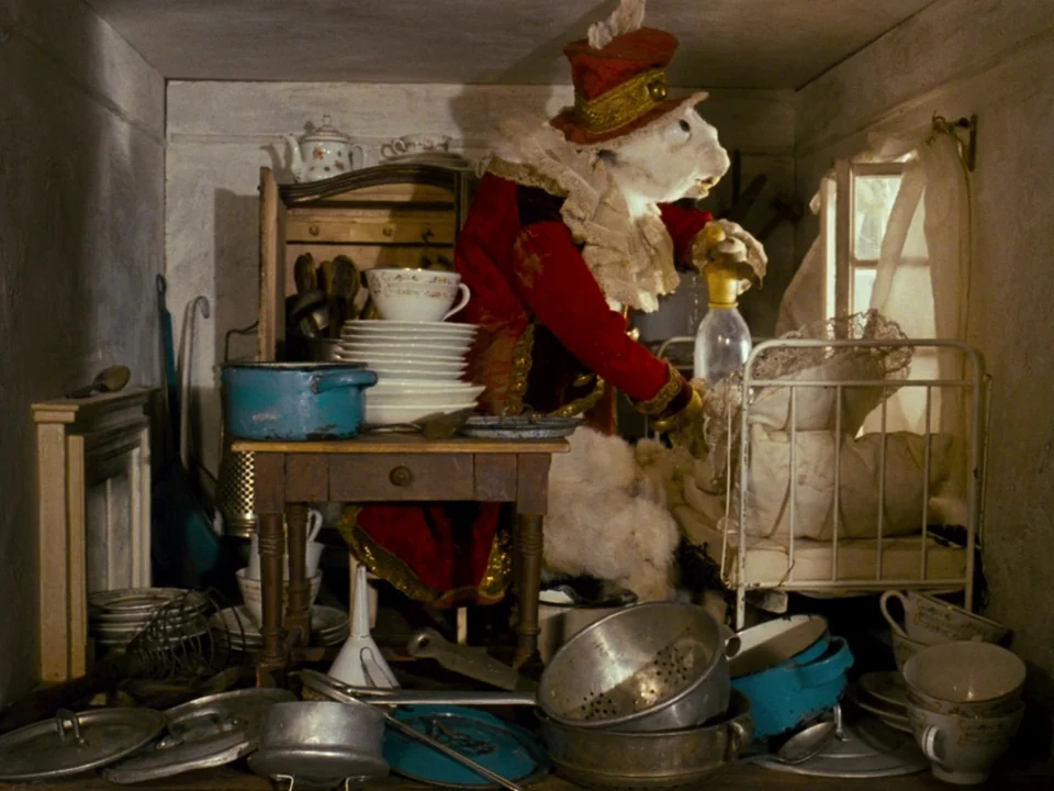 Alice (1988) movie still: medium — A cluttered miniature room filled with stacked dishes, pots, pans, and a toy bed. A white rabbit dressed in a…