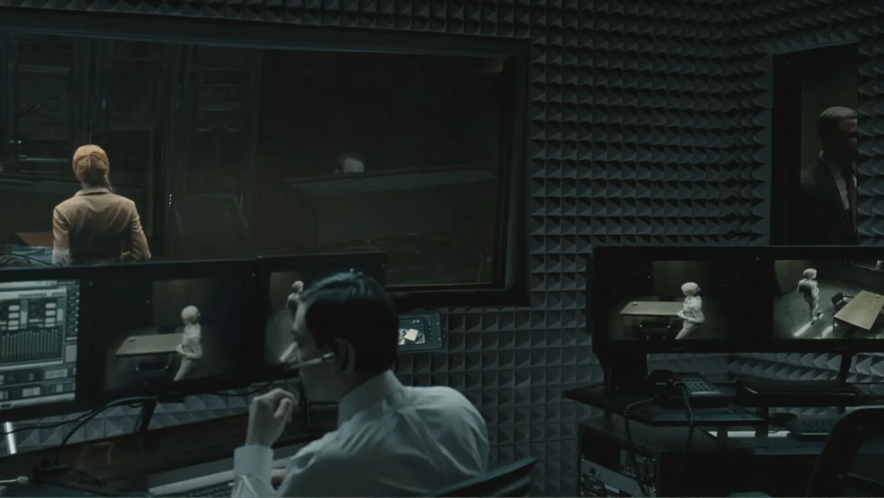 Salt (2010) movie still: medium — A dark surveillance room features walls covered in gray acoustic foam panels. A technician sits at a desk…