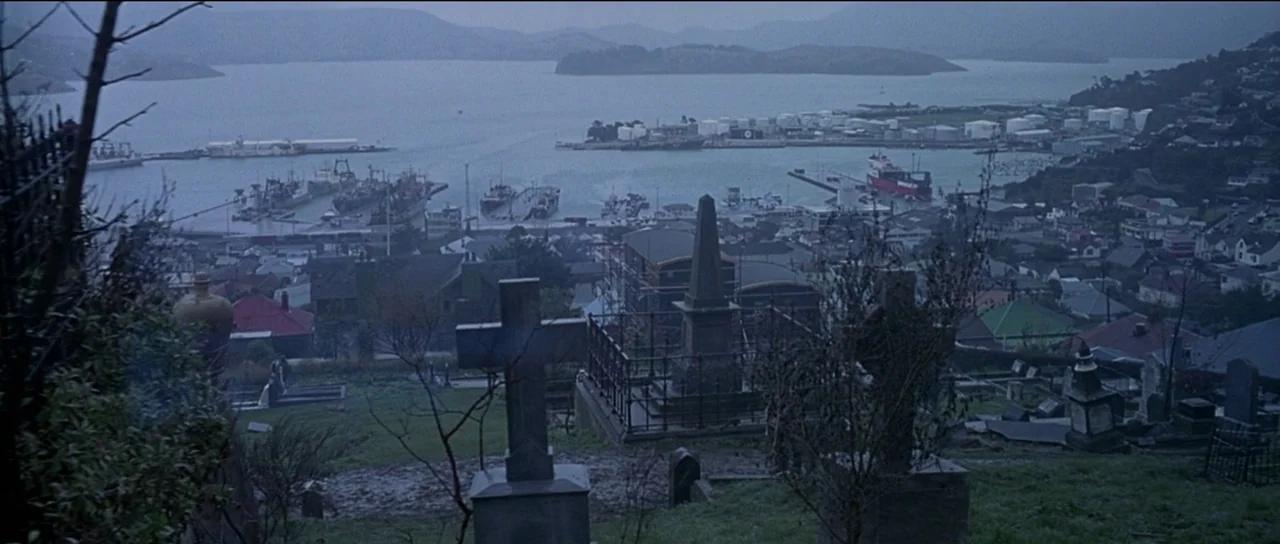 The Frighteners (1996) movie still: establishing — A quiet cemetery with stone markers sits on a grassy hill overlooking a harbor. Numerous…