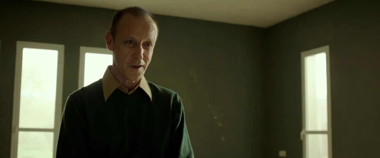 Big Bad Wolves (2013) movie still: medium — A sparsely furnished room features olive green walls and three bright rectangular windows. A mature man…