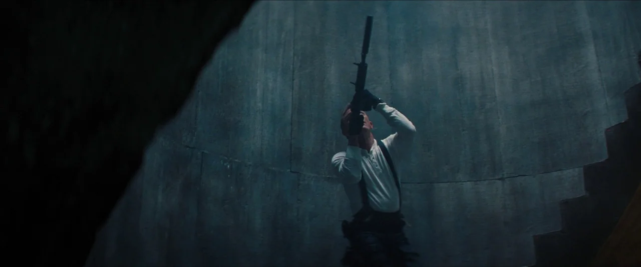 No Time To Die (2021) movie still: fullbody — A curved, windowless concrete stairwell creates a vertical, enclosed environment. A man in a white…