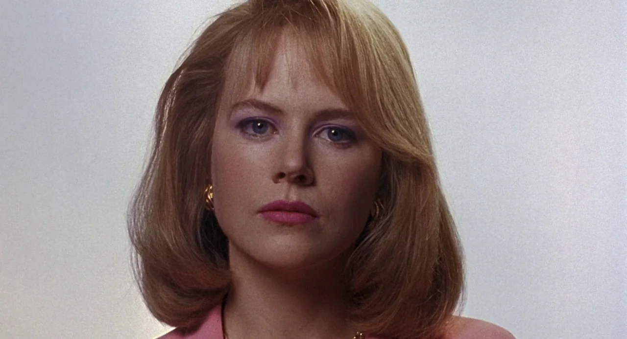 To Die For (1995) movie still: closeup — A woman stands before a plain white background in an interior space. She stares directly into the camera…