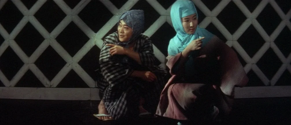 An Actor’s Revenge (1963) movie still: medium — Two people crouch before a diamond-patterned plaster wall at night. The pair gestures toward the…