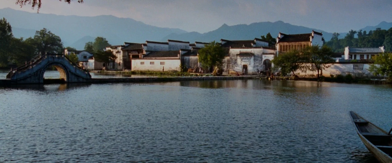Crouching Tiger, Hidden Dragon (2000) movie still: establishing — A traditional Chinese village with white-walled architecture sits behind a calm,…
