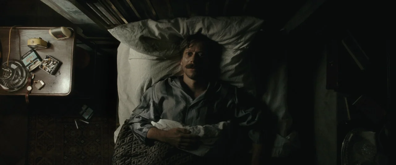 Chicken With Plums (2011) movie still: medium — A dimly lit bedroom features an overhead view of a man resting in a bed. An unmade nightstand sits…