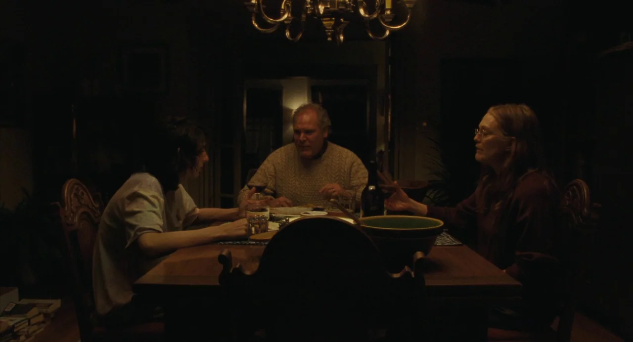 When You Finish Saving The World (2022) movie still: medium — Three people sit at a wooden dining table under an overhead chandelier at night. They…