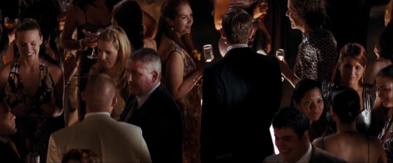 Quantum of Solace (2008) movie still: medium — A crowded indoor party space filled with guests in evening attire. Multiple people stand and converse…