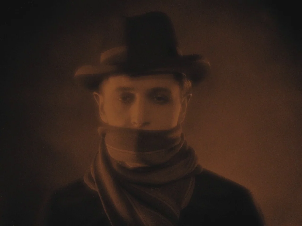 The Lodger (1927) movie still: closeup — A man in a dark hat and scarf stands against a dark background. He faces the camera directly while his…