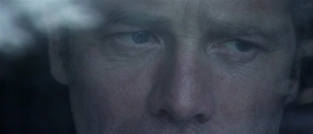 Session 9 (2001) movie still: closeup — The frame shows a tight shot of a middle-aged man's face from a car. Reflections and blur are visible on the…