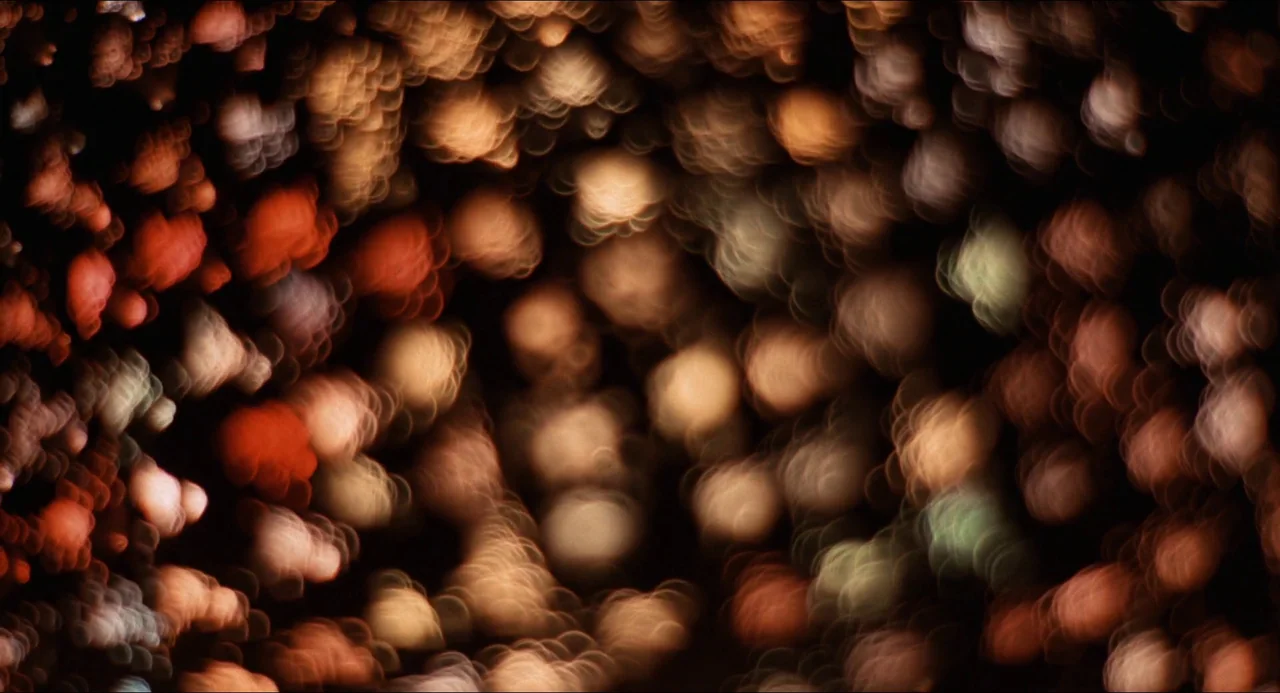 Medium Cool (1969) movie still: establishing — A dark night scene filled with dense, circular out-of-focus highlights. These abstract light spots…