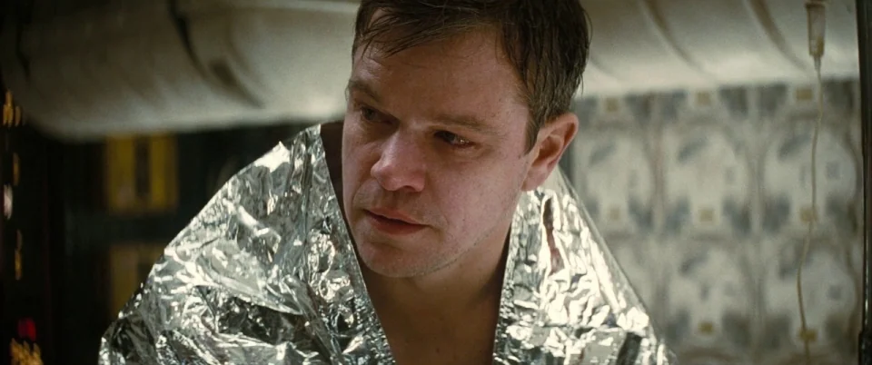 Interstellar (2014) movie still: closeup — A dimly lit interior of a sterile, metallic vessel with repetitive circular patterns on walls. A man sits…