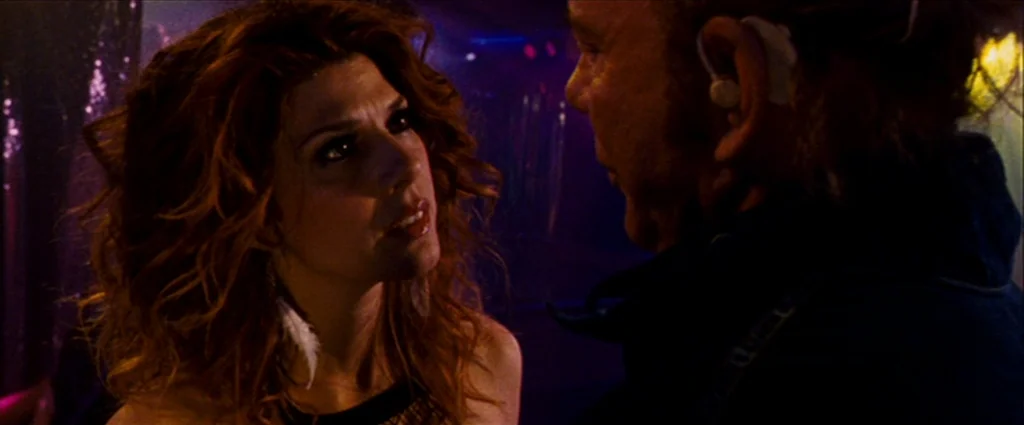 The Wrestler (2008) movie still: medium — A dark, dimly lit club interior with purple and magenta ambient lighting throughout. A woman with long…