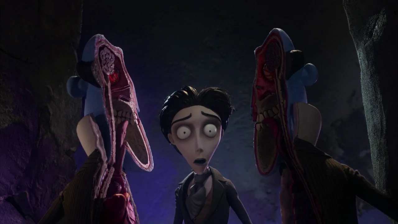 The Corpse Bride (2005) movie still: medium — A dark subterranean space with rock walls surrounds a man. He stands between two anatomically…