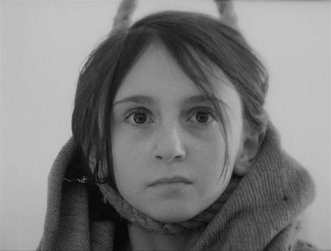 The Ascent (1977) movie still: closeup — A close-up shot showing a child against a stark, light-colored backdrop. The child is wrapped in a thick,…