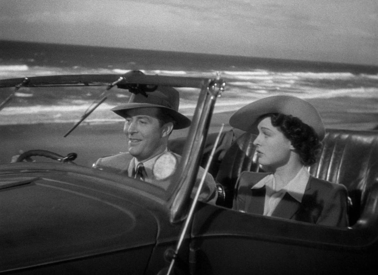 The Uninvited (1944) movie still: medium — A man and woman drive along a dark coast in an open-top convertible car. The ocean waves crash on the…