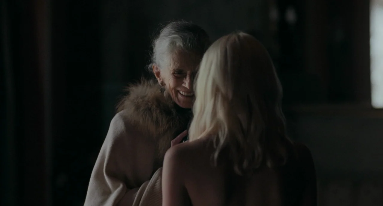La Abuela (2021) movie still: medium — A dimly lit room provides a dark background for the two women interacting. An older woman with grey hair…