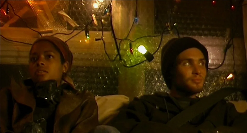 28 Days Later (2002) movie still: medium — A dimly lit room features walls covered in reflective, textured insulation panels. A man and a woman sit…