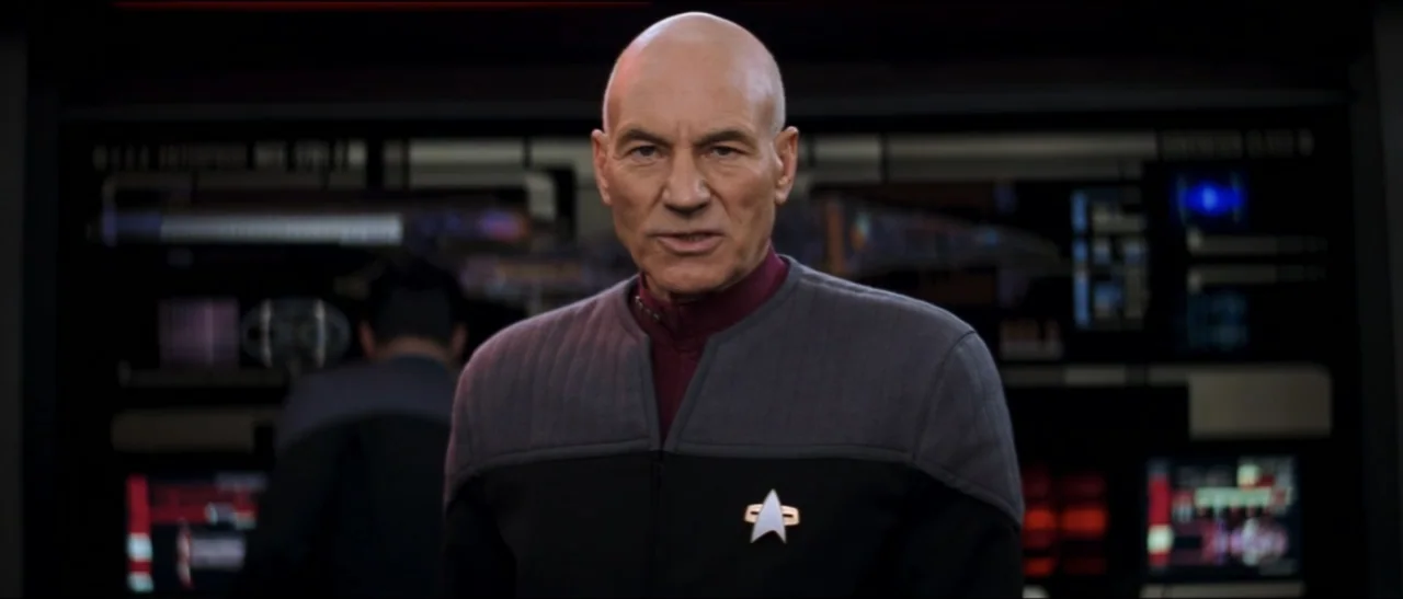 Star Trek: Nemesis (2002) movie still: medium — A high-tech control deck features dark panels with glowing blue and red status readouts. A bald man…